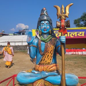A large, colorful statue of Lord Shiva seated in a cross-legged position, with a raised hand in a gesture of blessing.