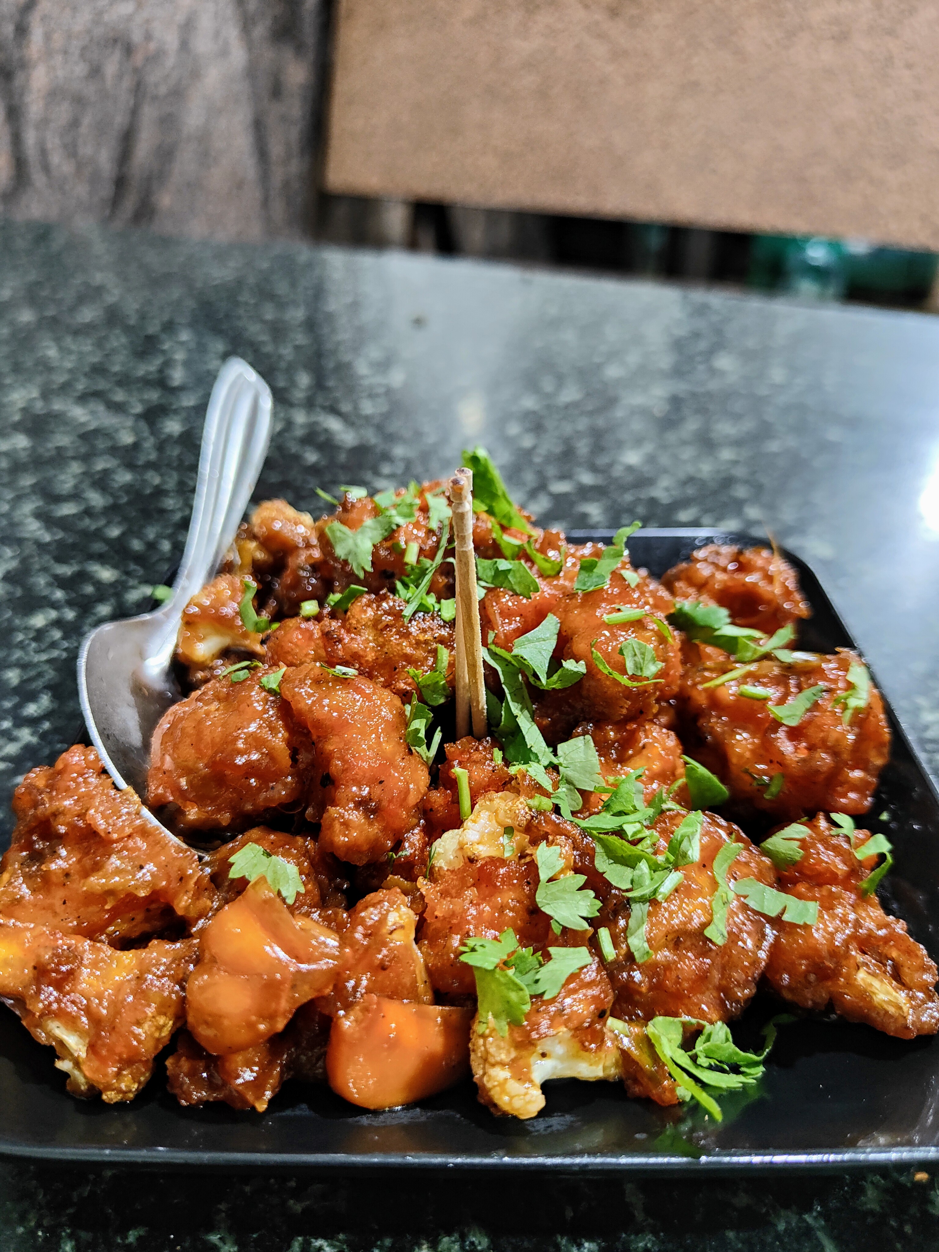 Close-up of Gobi Manchurian — crispy battered cauliflower in a glossy reddish-orange sauce, topped with fresh green cilantro.