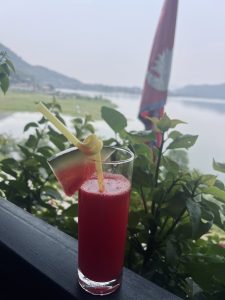 A refreshing red drink served in a tall glass, garnished with a slice of watermelon and a twist of yellow citrus. 