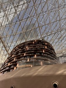 A modern library interior featuring a curved, multi-tiered bookshelf filled with books.