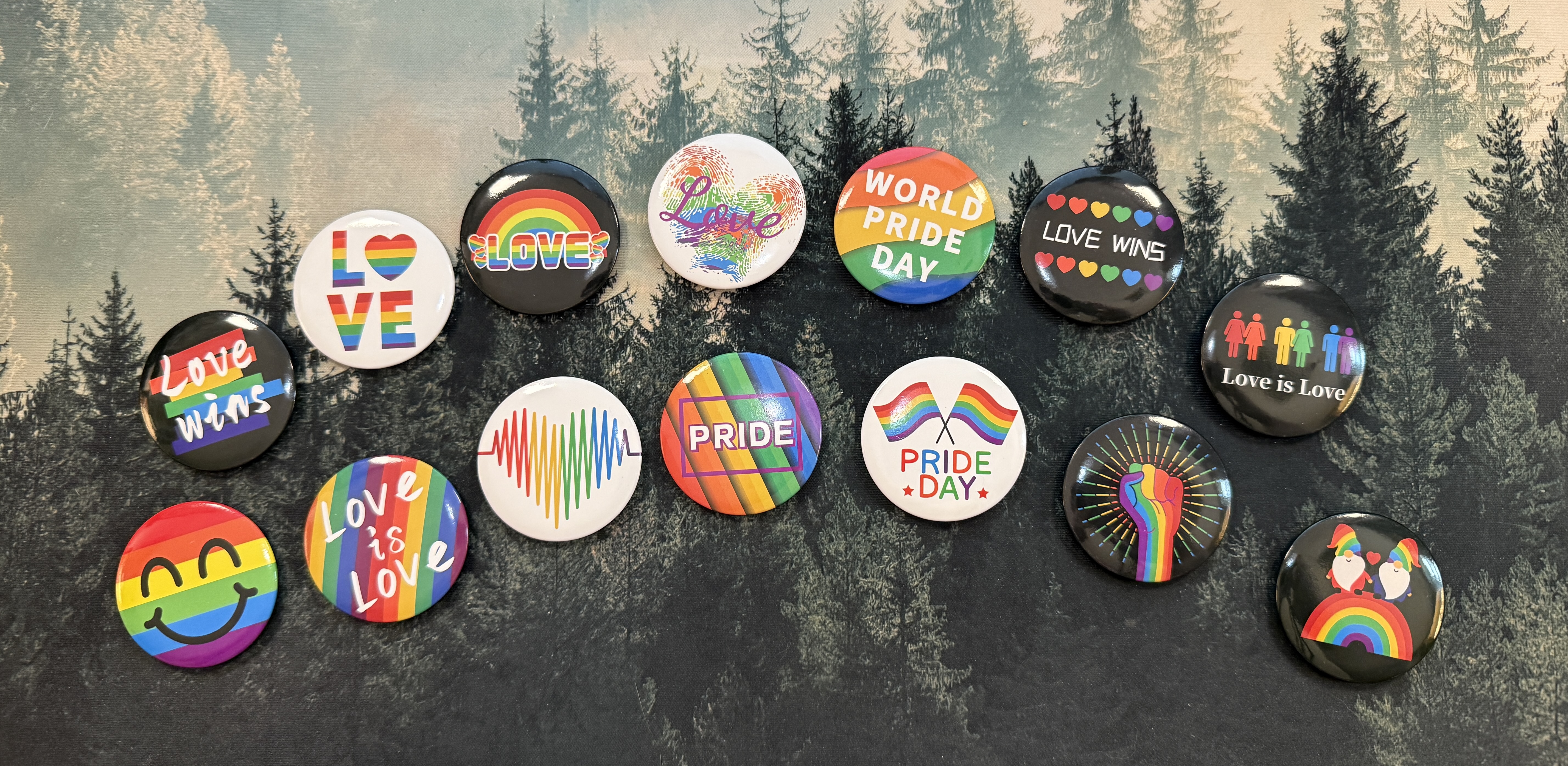 A display of pride pins arranged in an arc on a desk. They include phrases like "Love Wins" and "Love is Love" and "Pride." #ShareYourPride2025