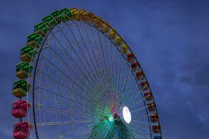 A brightly lit Ferris wheel against a twilight sky, featuring colorful illuminated cabins in vibrant colors.