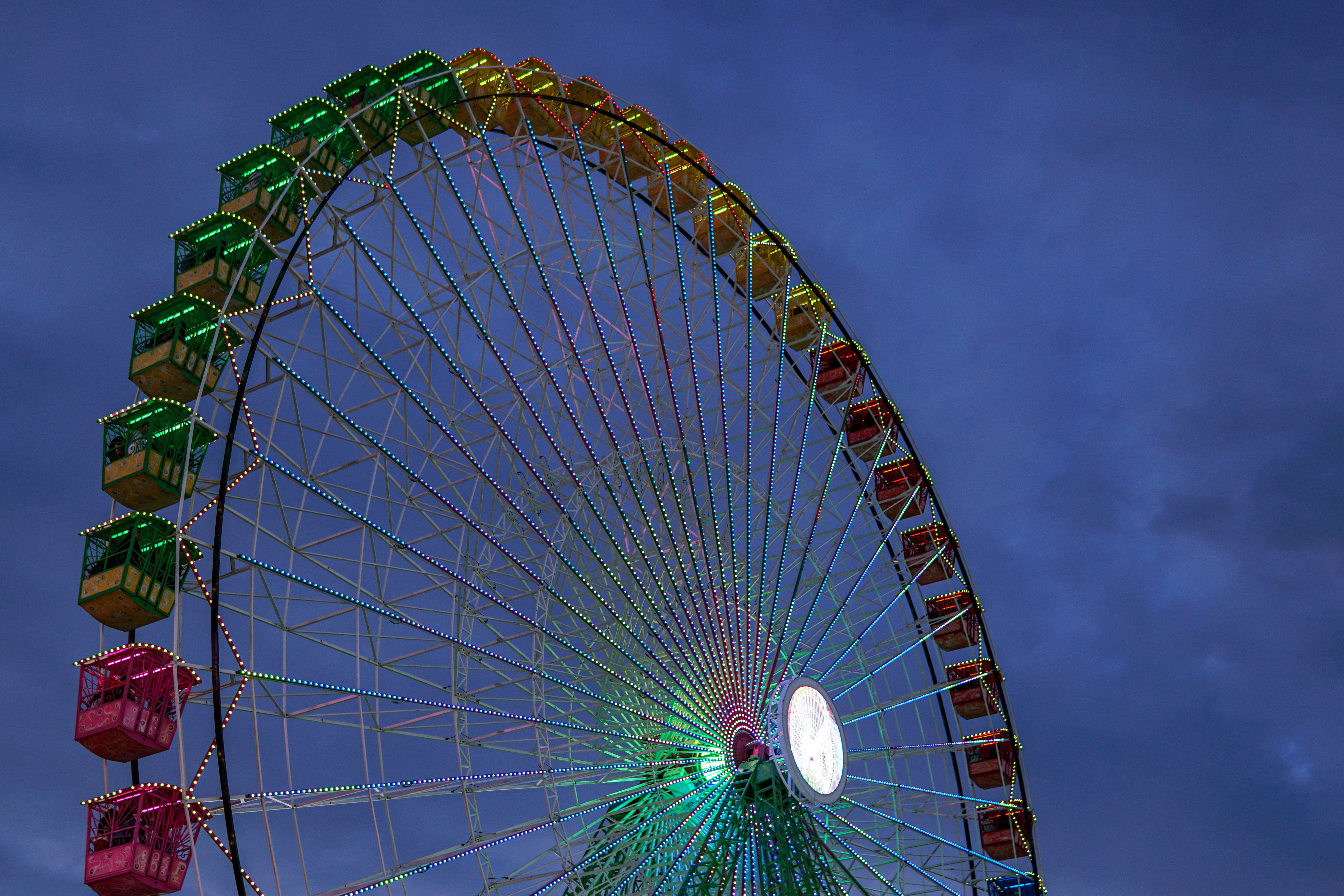 A brightly lit Ferris wheel against a twilight sky, featuring colorful illuminated cabins in vibrant colors.