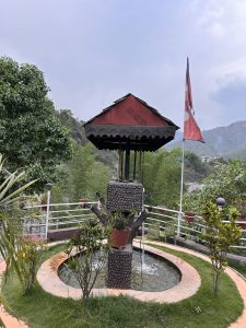 A scenic outdoor area featuring a decorative water fountain designed to resemble a tree, surrounded by greenery and plants in pots.
