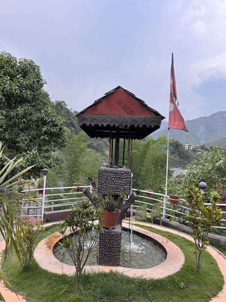 A scenic outdoor area featuring a decorative water fountain designed to resemble a tree, surrounded by greenery and plants in pots.