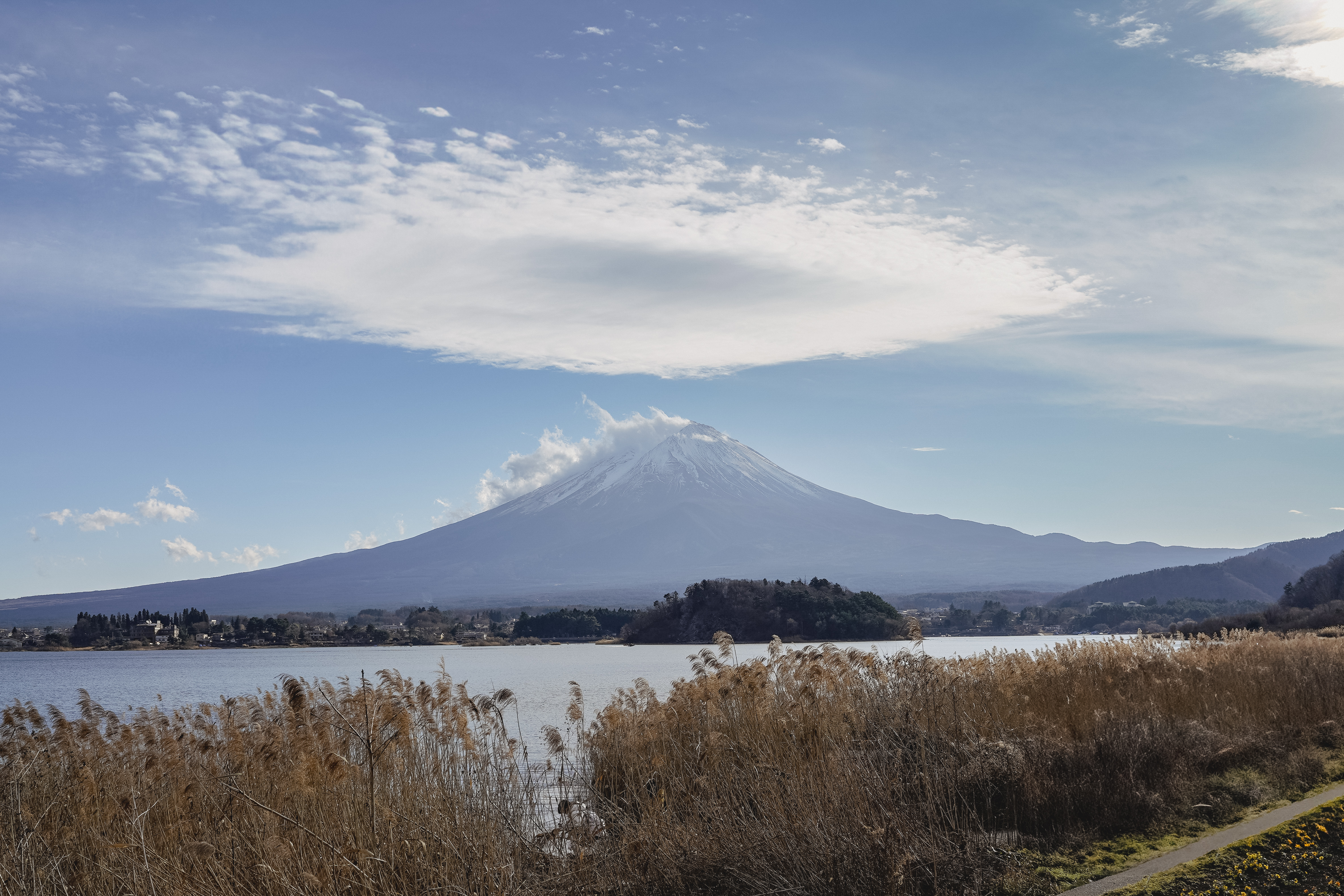 A scenic view of Mount Fuji rising majestically against a clear blue sky, partially covered by clouds.