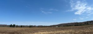Open field recently turned over and fertilized for the spring planting.  There's a farmstead in the distance on the other side of the field.
