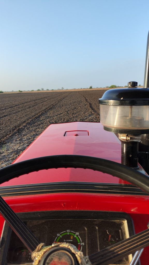 A view from the driver’s seat of a red tractor overlooking a plowed field.