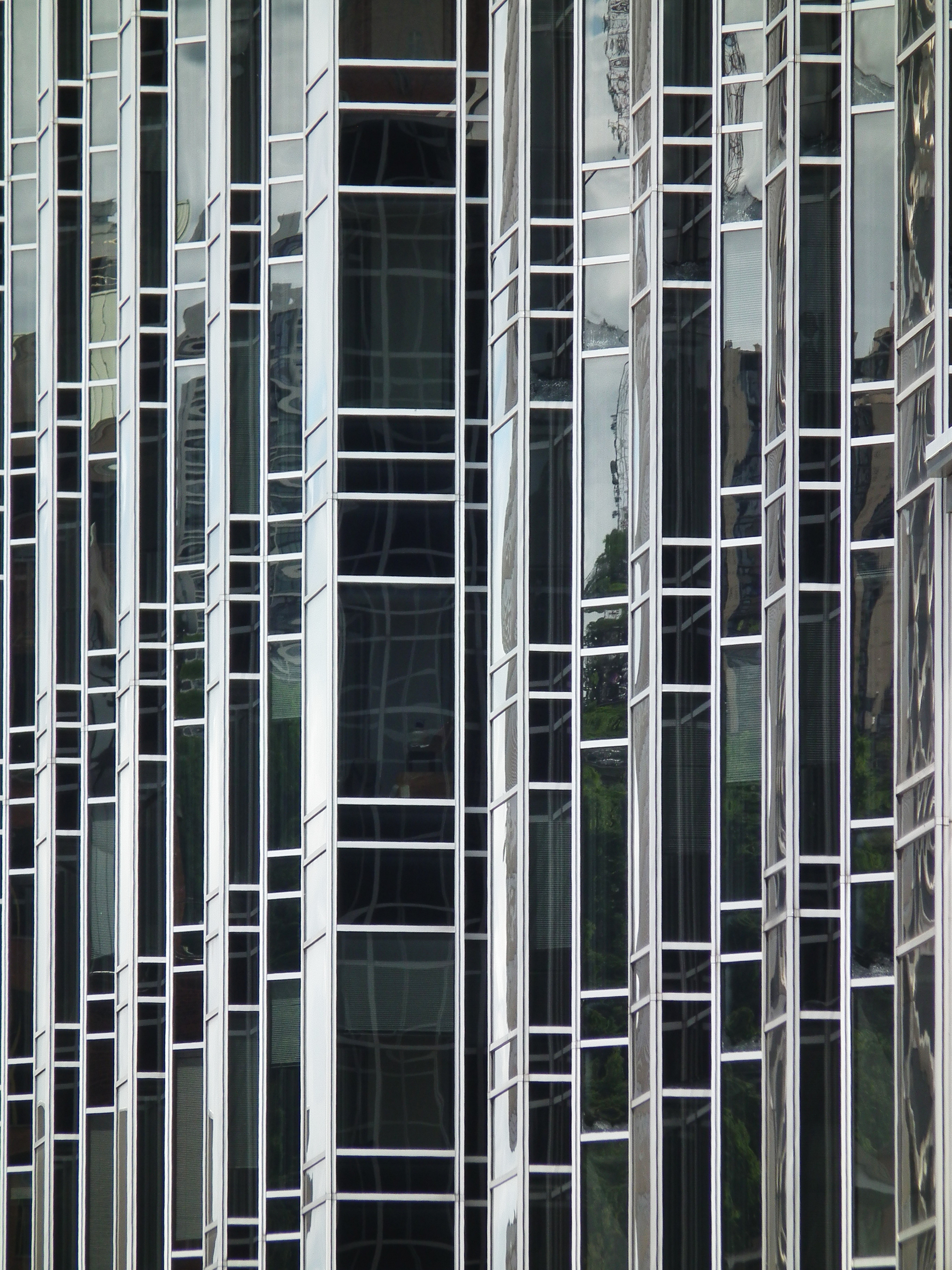 A close-up view of a modern glass building facade featuring vertical reflective panels and metal framing.