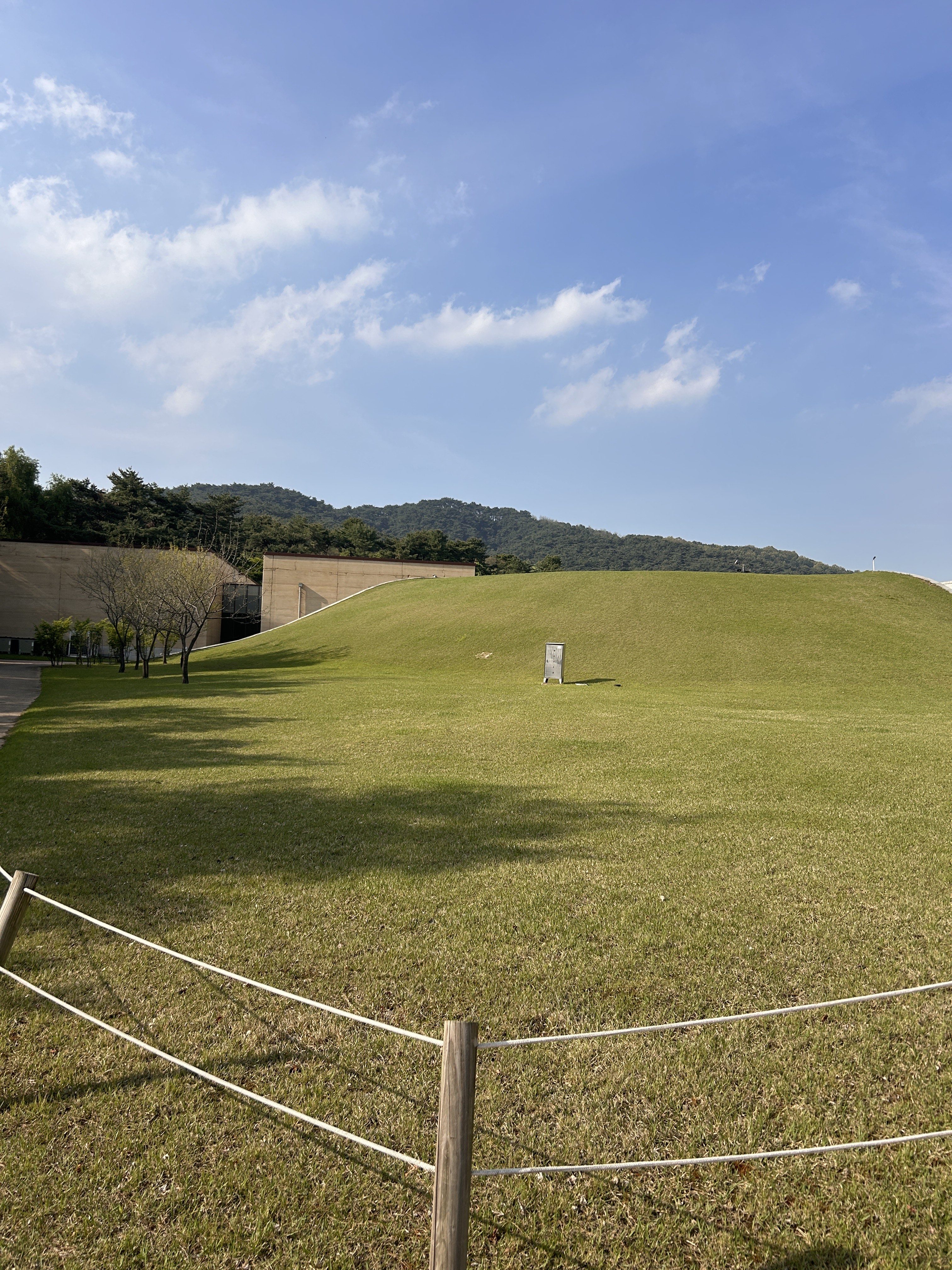 A spacious green lawn stretches across the foreground, with a gently sloping hill in the background.