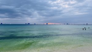 A serene view of the ocean under a cloudy sky, with various sailboats featuring blue sails in the distance
