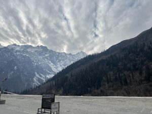Snow-capped mountains seen from the ground under a slightly cloudy sky with light, misty weather.