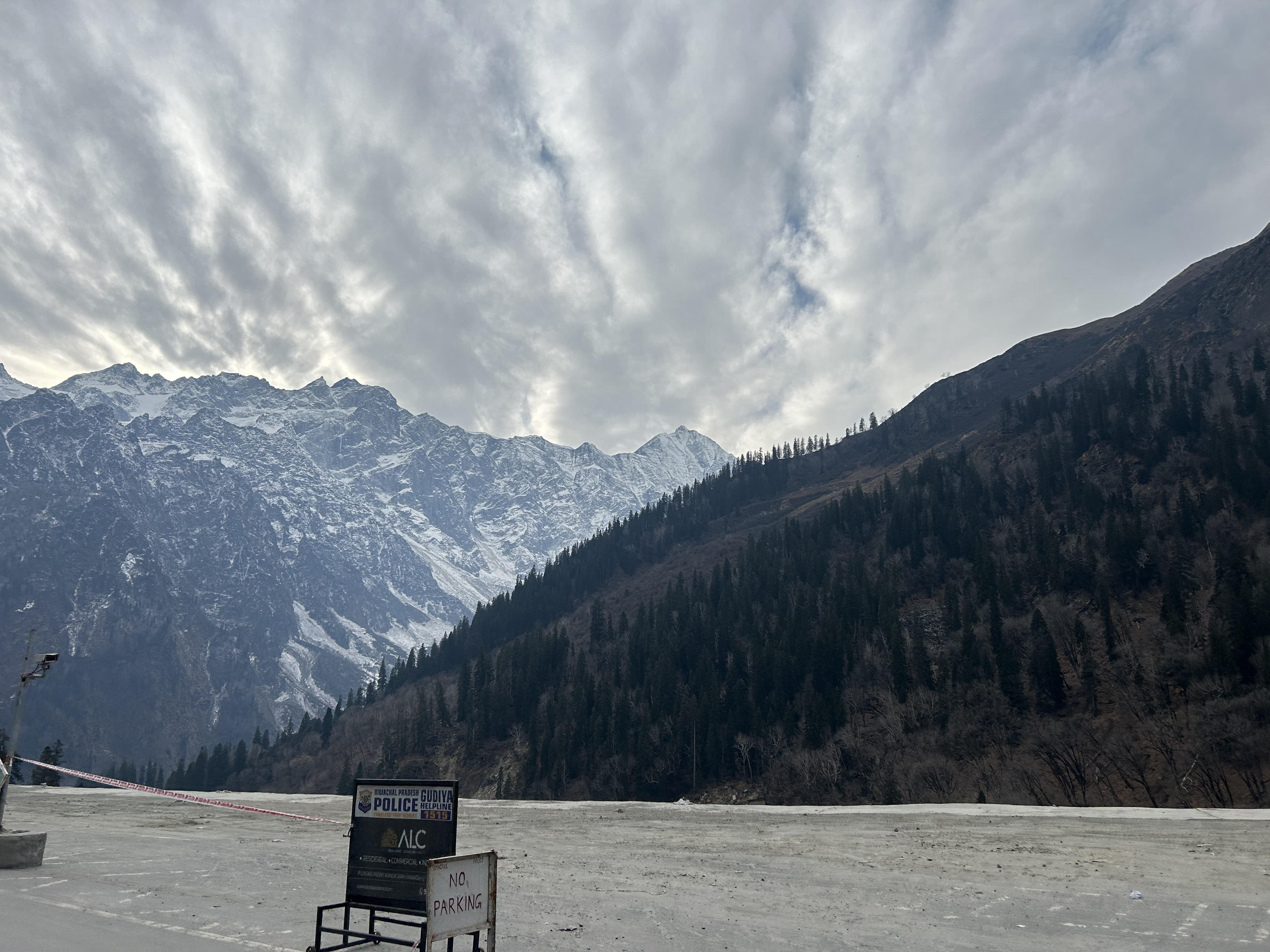 Snow-capped mountains seen from the ground under a slightly cloudy sky with light, misty weather.