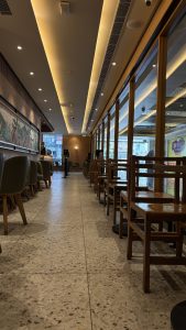 A modern café interior featuring a long, narrow space with wooden chairs and tables arranged along either side. 