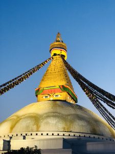 

A close-up view of a large Boudha stupa adorned with colorful prayer flags against a clear blue sky.