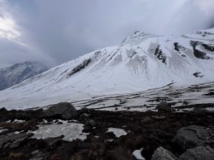 A snowy mountain landscape under a cloudy sky, showcasing steep snow-covered slopes with visible rocky outcrops.