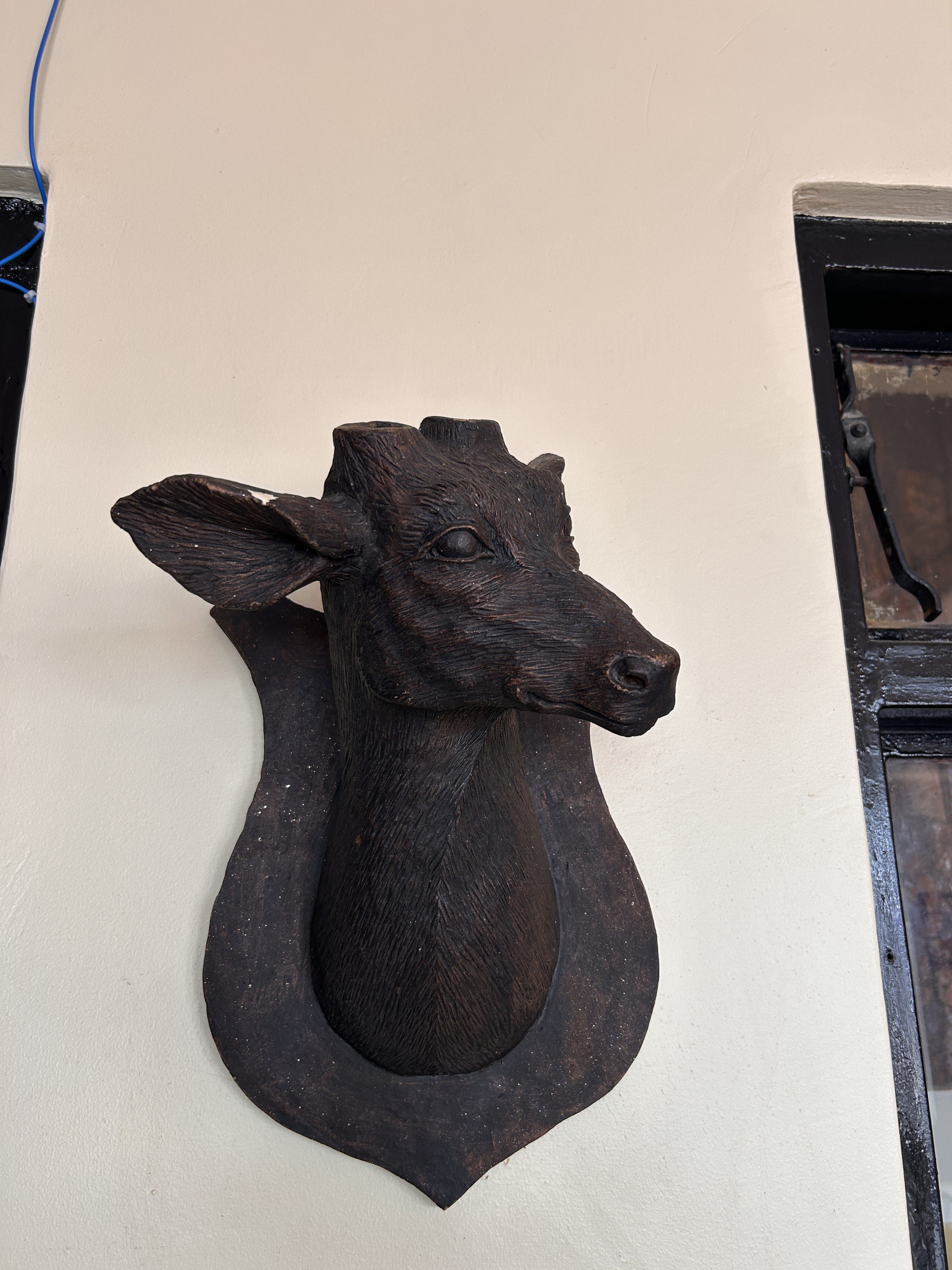 A mounted wooden sculpture of a deer's head is displayed on a wall.