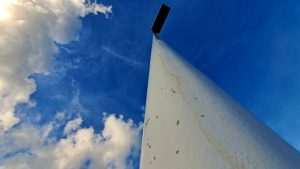 A close-up shot of a white solar post, slightly weathered with hints of rust, set against a backdrop of a cloudy sky.