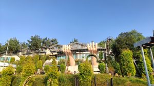 A scenic view of a hillside resort, featuring large sculptures of hands prominently in the foreground.