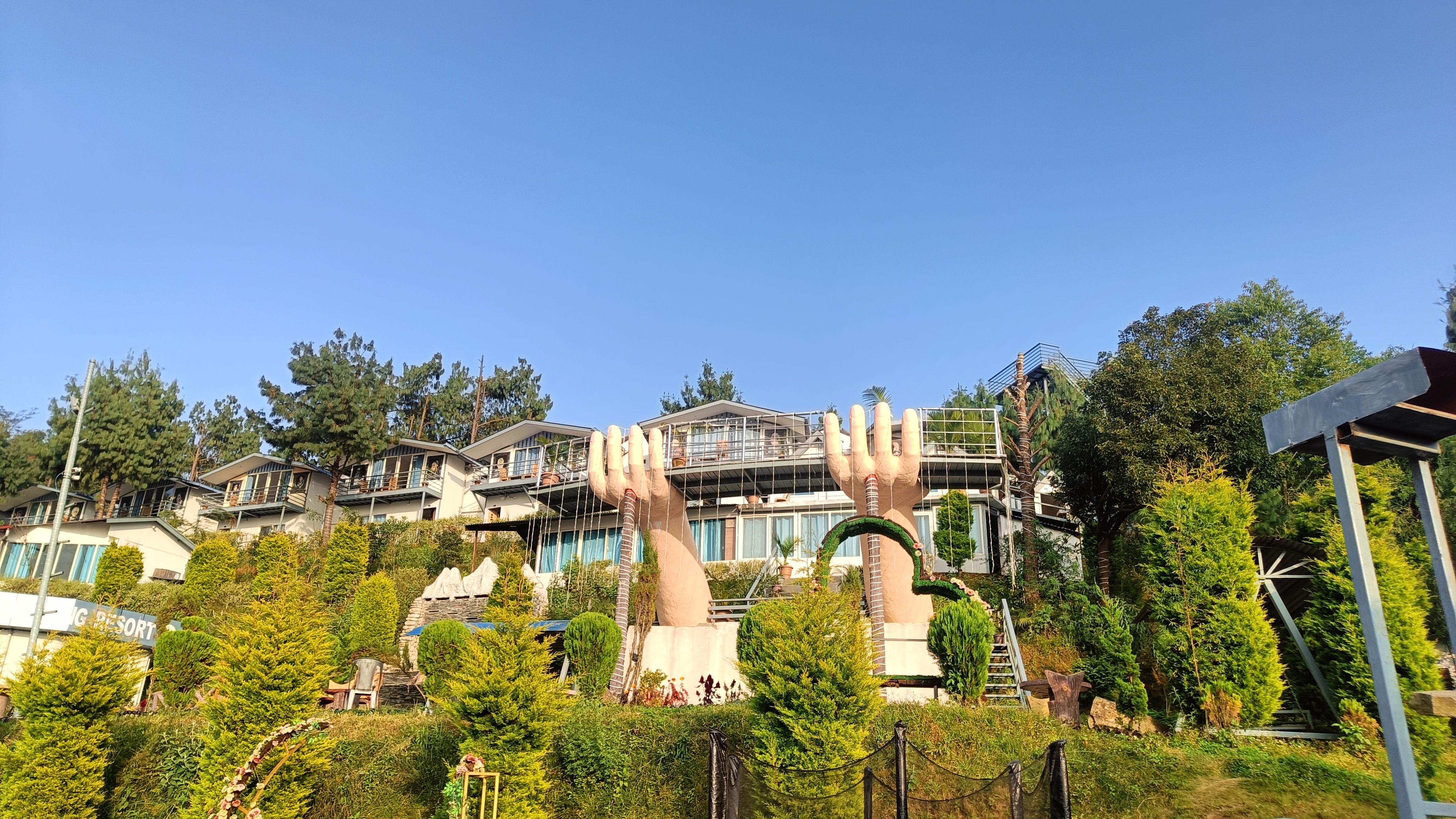 A scenic view of a hillside resort, featuring large sculptures of hands prominently in the foreground.
