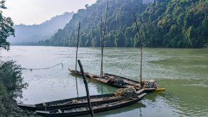 A tranquil river scene features several wooden boats moored at the water’s edge
