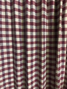 A close-up view of a fabric with a classic checkered pattern, featuring alternating squares of deep burgundy and cream colors