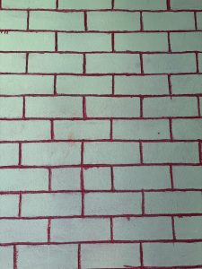 A textured wall featuring a pattern of light green bricks outlined in red mortar. 