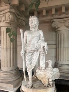 A white marble statue of a bearded man standing confidently, holding a staff in his right hand.