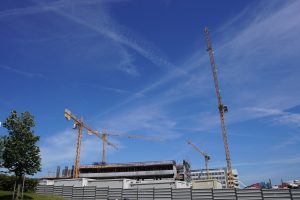 A construction site with several yellow cranes towering above a partially built structure against a clear blue sky.