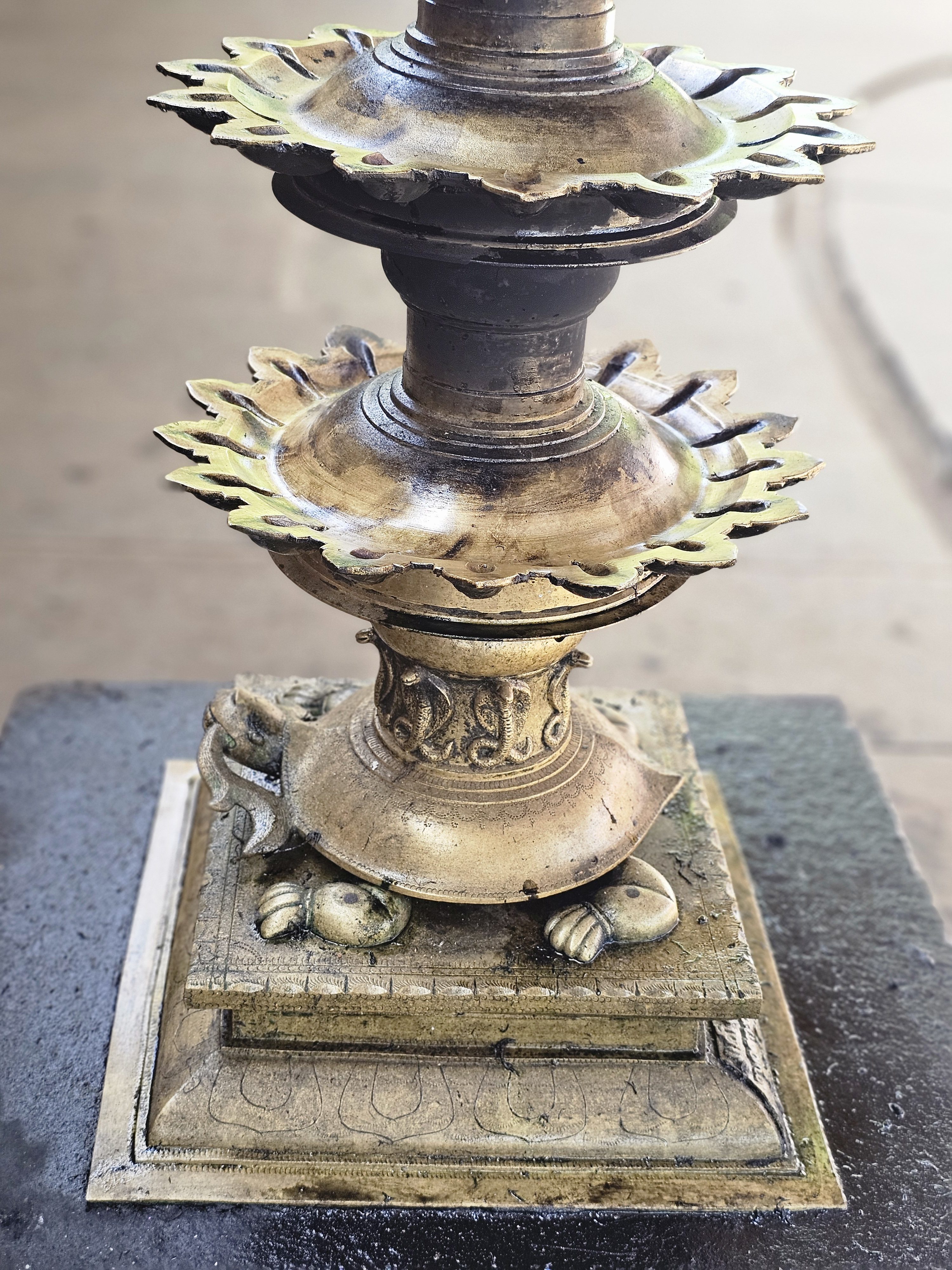 Close-up shot of a traditional Indian bronze oil lamp, which is commonly used in temples in Kerala. The lamp features a tiered design with two oil basins, each adorned with petal-like edges, and it stands on a square base with intricate carvings and small feet resembling a tortoise. Captured from Thirumandhamkunnu Temple, Angadippuram, Malappuram.