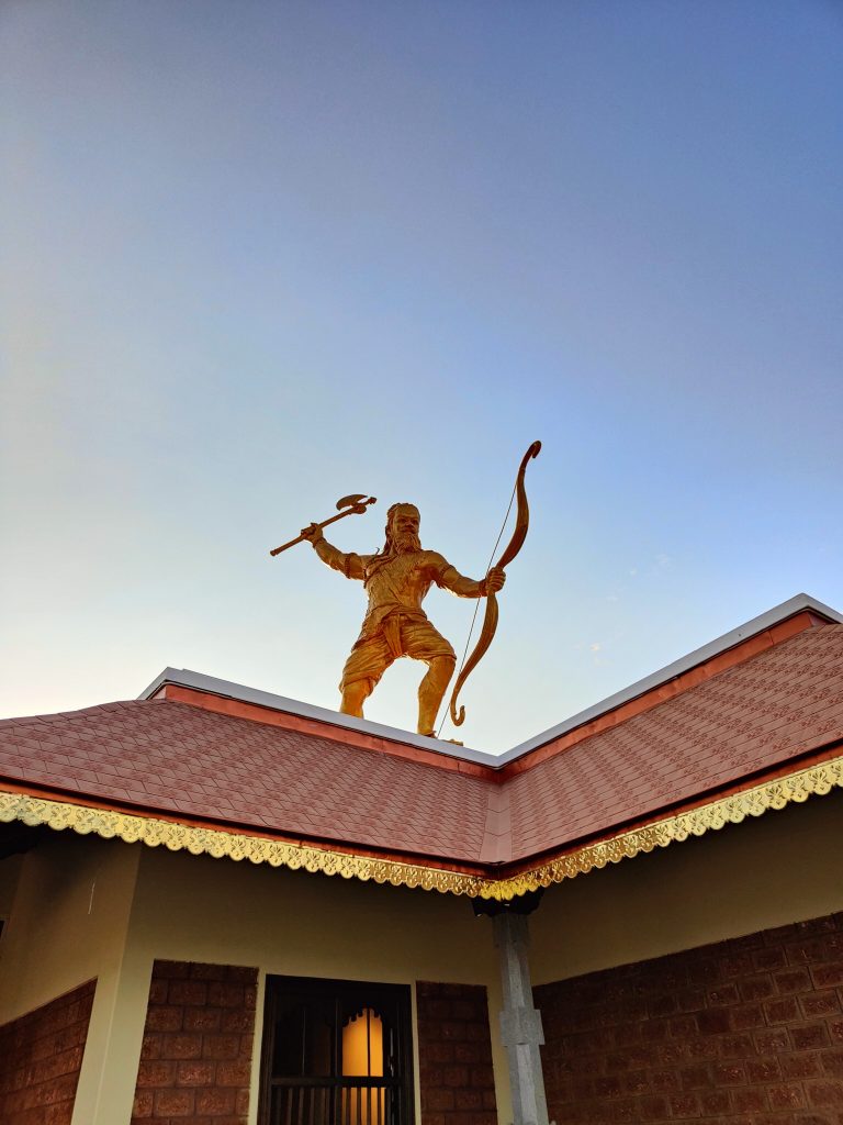 A large golden statue of a warrior stands atop a building. The figure holds a bow in one hand, with an axe resting in the other, symbolizing strength and readines