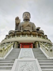

A large bronze statue of Buddha sits atop a circular platform, with one hand raised in a gesture of blessing. 