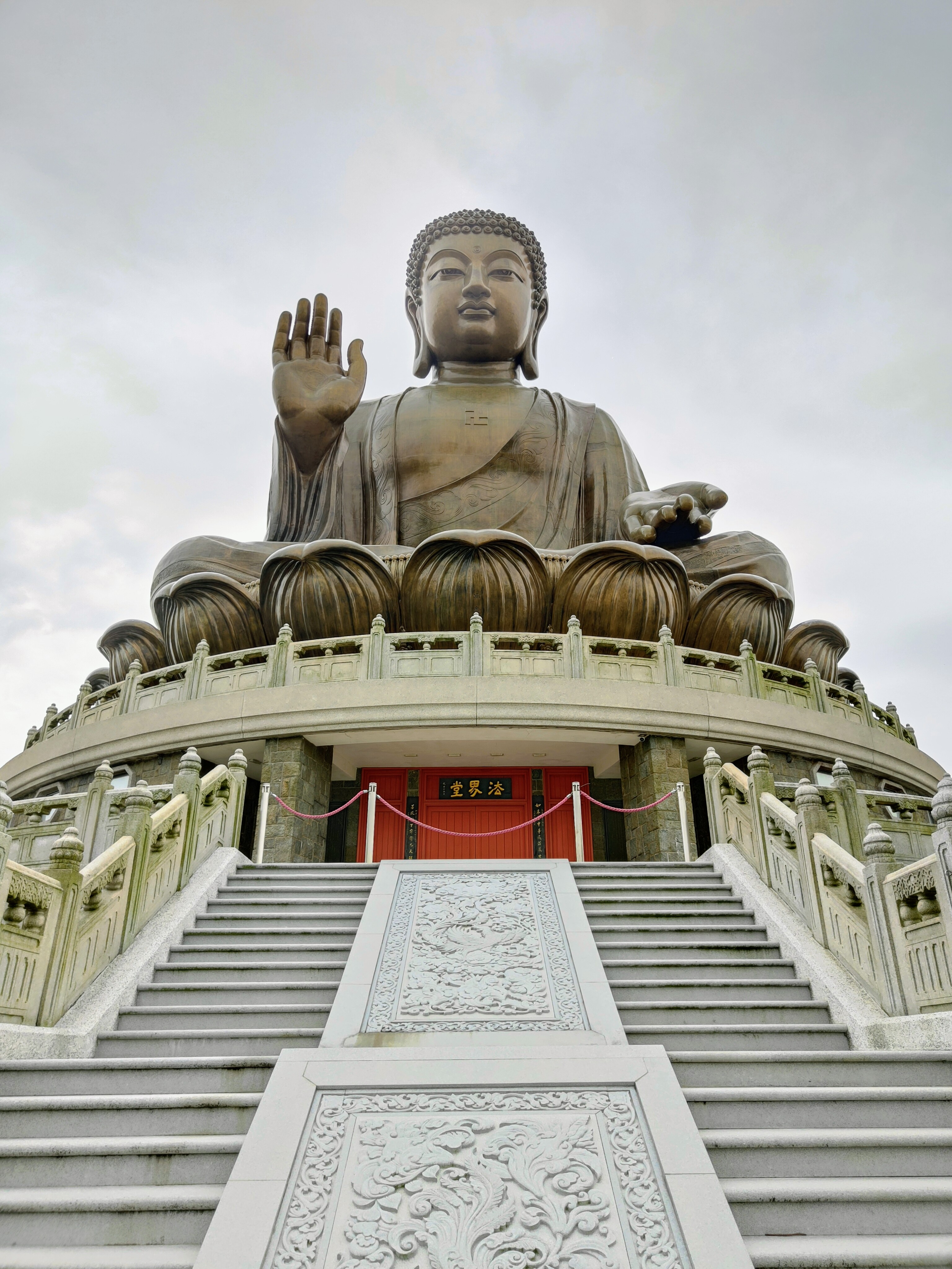 A large bronze statue of Buddha sits atop a circular platform, with one hand raised in a gesture of blessing.