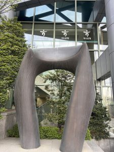 A large, modern sculpture resembling a curved arch stands in front of a glass building. 