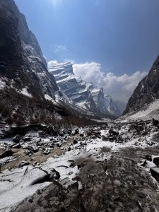 A breathtaking view of a valley surrounded by towering snow-capped mountains under a bright blue sky.