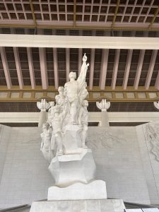 A large, white stone sculpture depicting a group of figures in a dramatic pose, with one figure raising an arm upward.