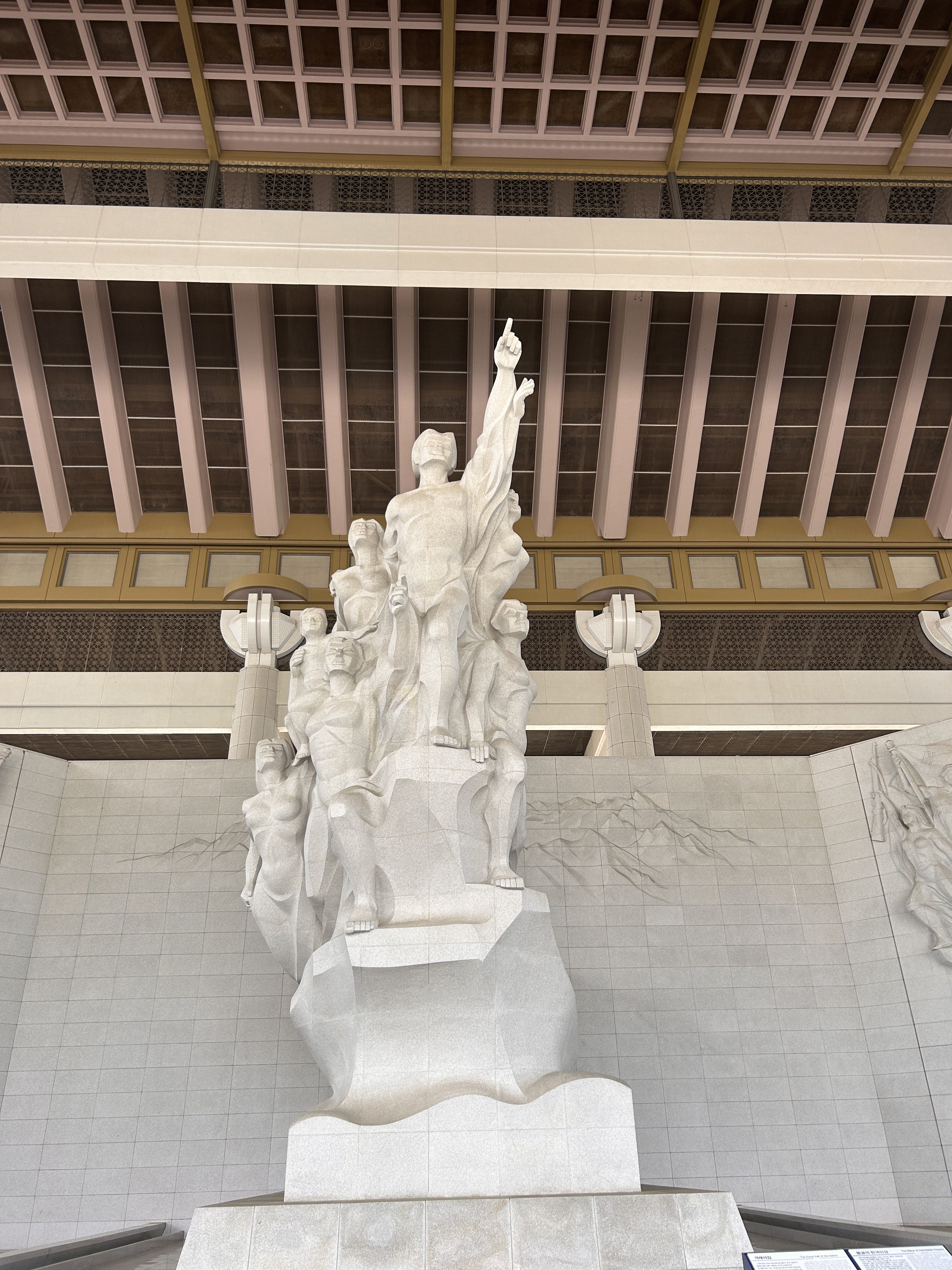 A large, white stone sculpture depicting a group of figures in a dramatic pose, with one figure raising an arm upward.