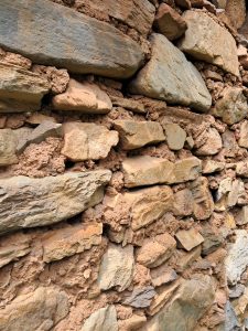 A close-up view of a textured stone wall made of various-sized rocks and clay. 