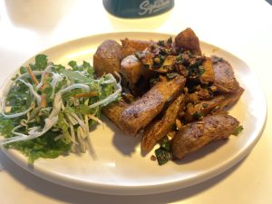 A plate featuring a serving of golden-brown, seasoned potato wedges, garnished with chopped herbs and spices. 
