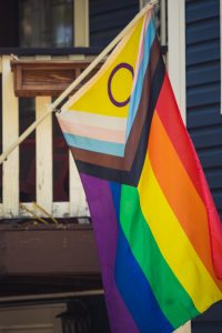Intersex Inclusive Pride flag hanging on a diagonal off a porch in front of a blue house 