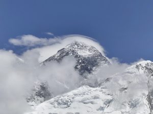 

A majestic snow-capped everest mountain peak rises into a clear blue sky, surrounded by wispy clouds. 