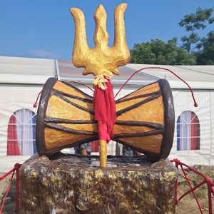
A large decorative installation featuring a golden trident atop a large drum, surrounded by colorful fabric.