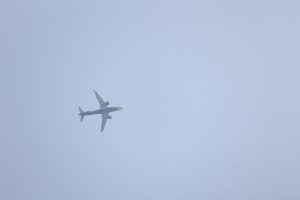An airplane flying in a clear blue sky, viewed from below, with its wings extended and a light gray background.