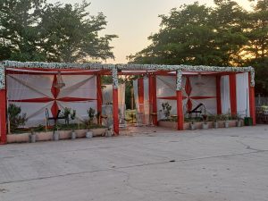 A decorated outdoor event space features two structures with red and white drapes, adorned with floral arrangements along the tops.
