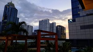 A city skyline at dusk featuring several high-rise buildings, some with illuminated windows.