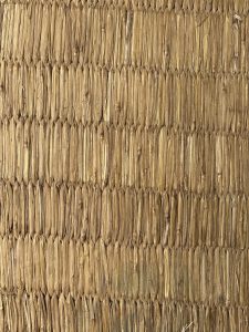 A close-up texture of tightly woven, dried plant material, showcasing rows of elongated, leaf-like strands arranged in a consistent pattern