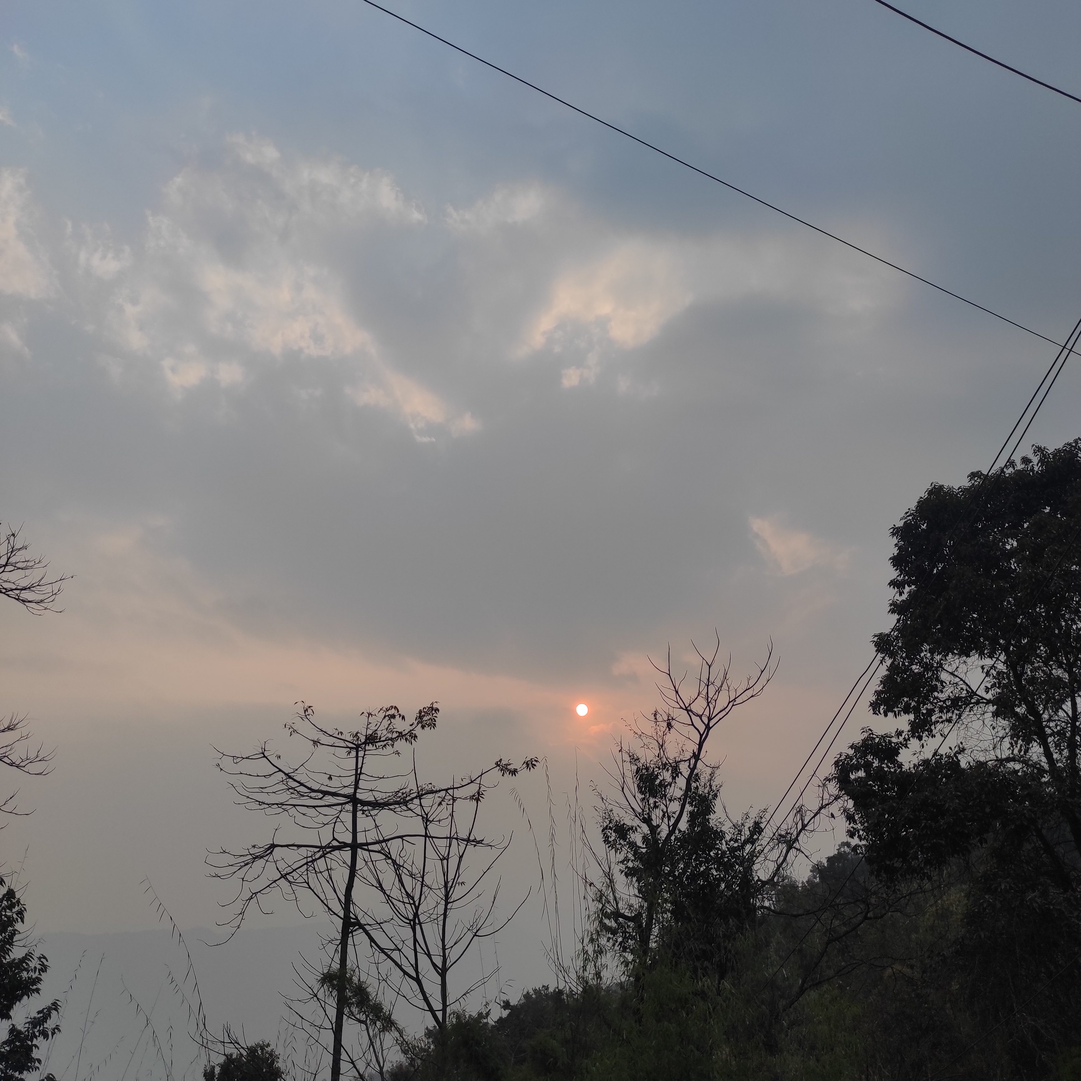 A hazy sunset is visible behind clouds, with a soft orange sun partially obscured.