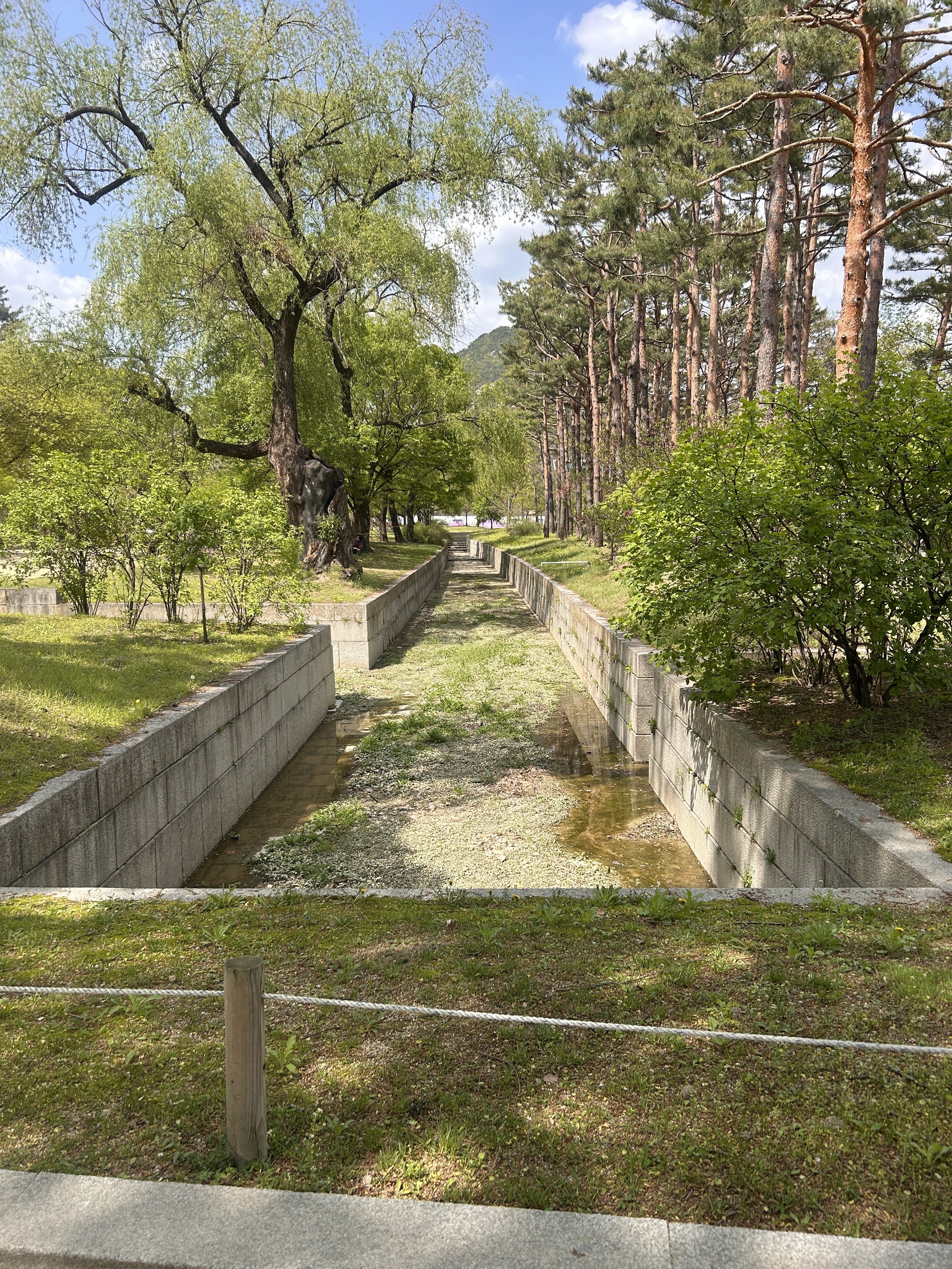 A serene landscape featuring a narrow, dry canal flanked by lush greenery