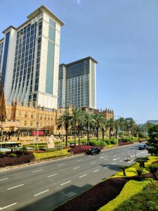 A stunning view of the iconic Londoner Macao, featuring its grand British-inspired architecture, well-maintained palm-lined roads, and luxurious high-rise towers under a clear blue sky.

