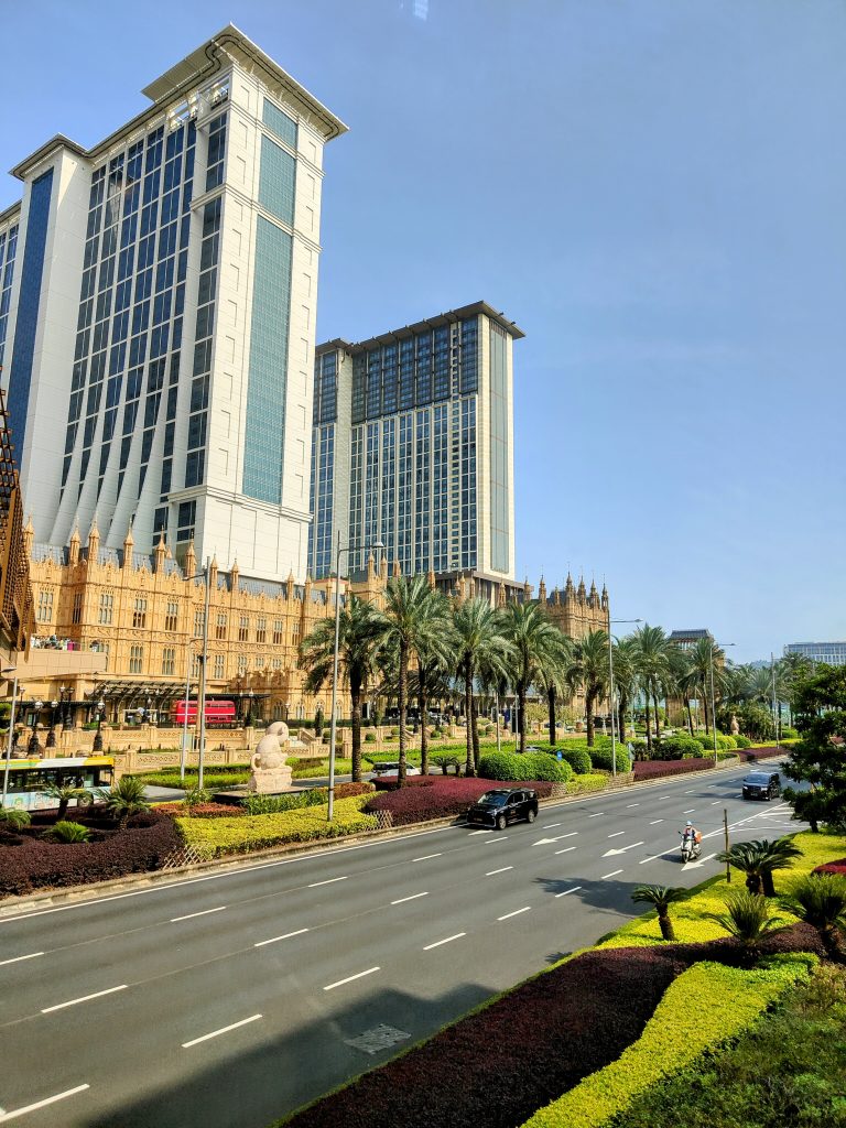 A stunning view of the iconic Londoner Macao, featuring its grand British-inspired architecture, well-maintained palm-lined roads, and luxurious high-rise towers under a clear blue sky.